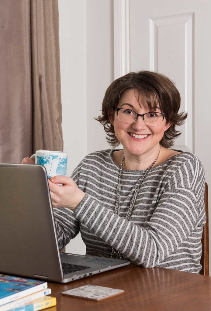 Elizabeth Harrin sitting at a table using a laptop computer holding a cup of tea