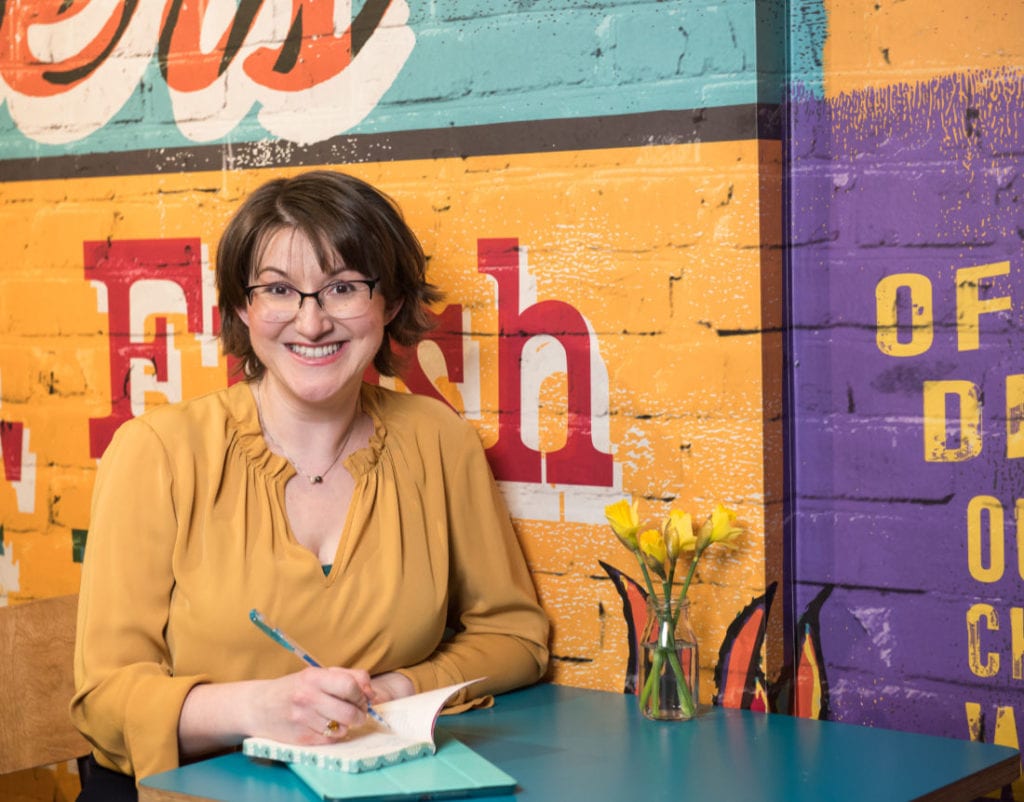 Elizabeth Harrin sitting at a table in front of a sign at a cafe