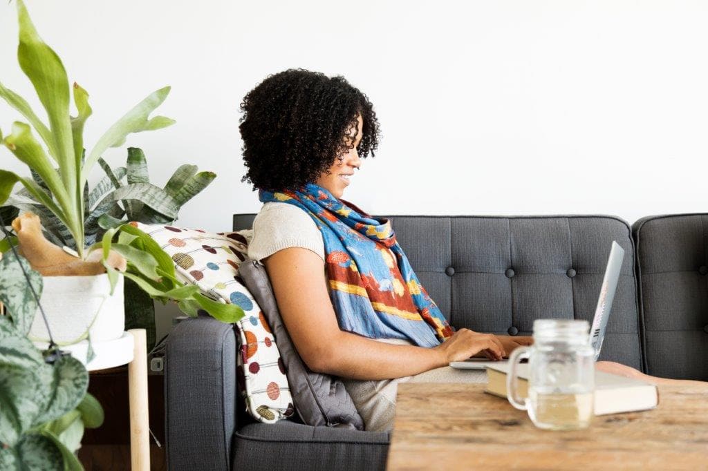 A woman sitting on a sofa using a laptop on her lap