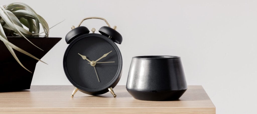 A pot that is sitting on a wooden table next to a clock