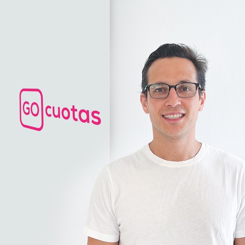 Cristina Rennella wearing glasses and a white T shirt next to his company logo.